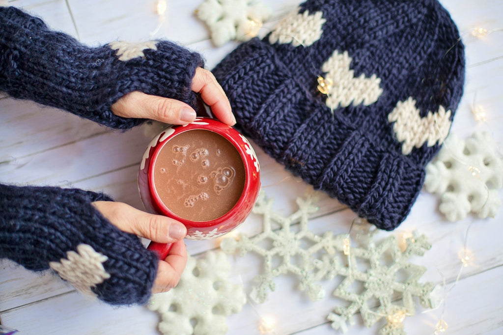 woman holding hot cocoa with knitted hat and mittens