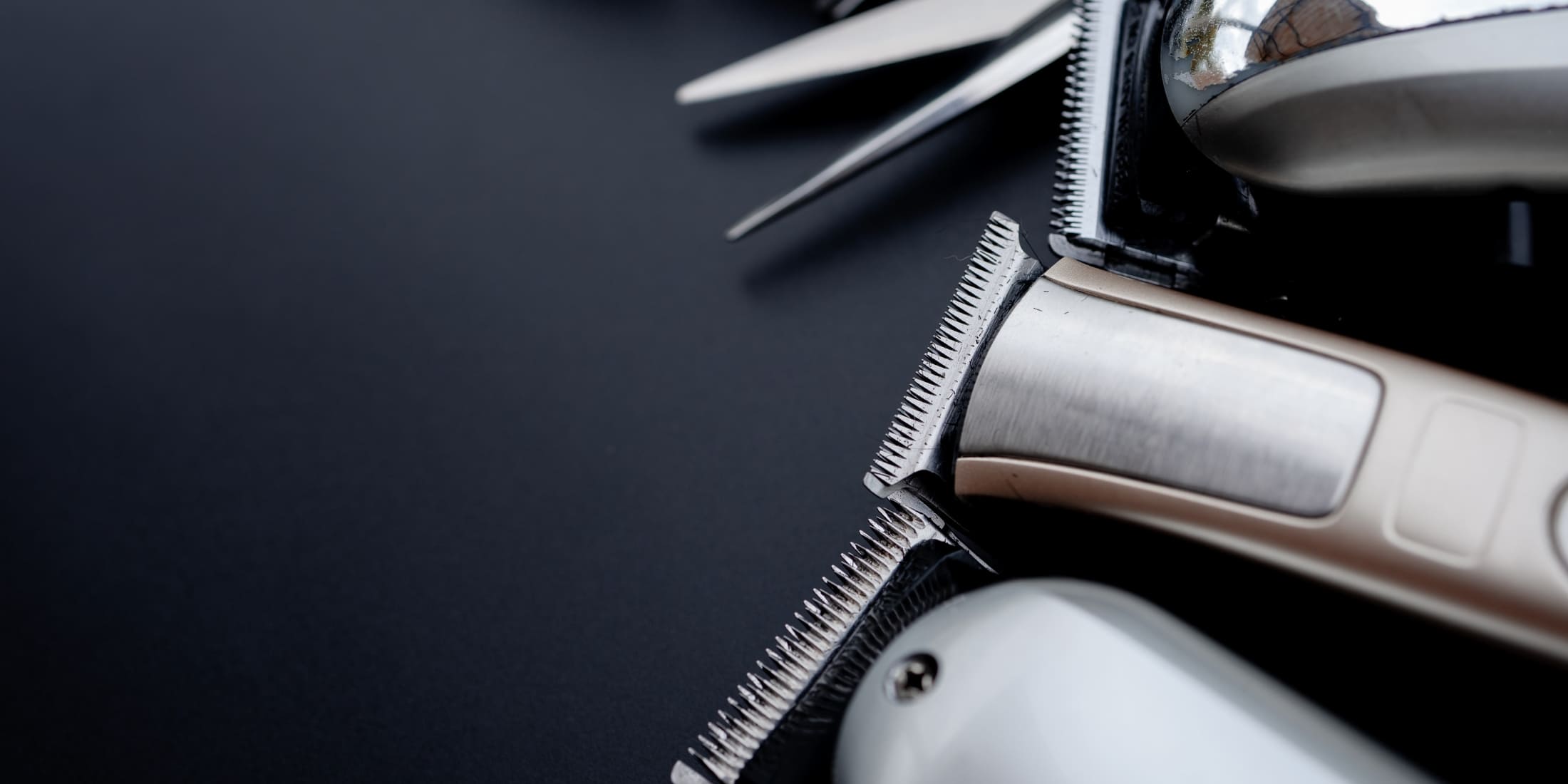 Close-up of three professional hair clippers on a black background, demonstrating how to clean hair clippers for optimal performance and hygiene.