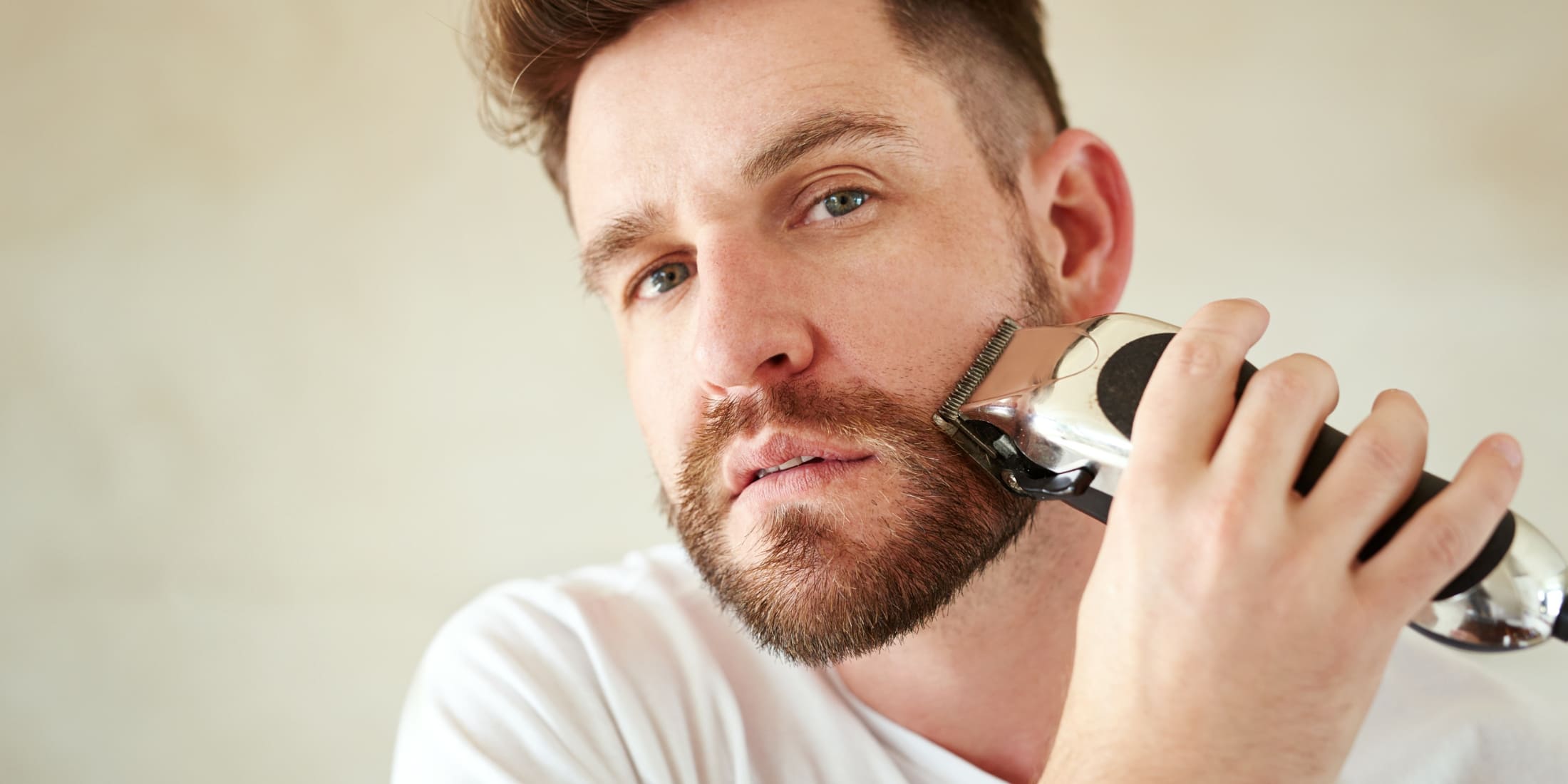 Bearded man using a trimmer to avoid common beard trimming mistakes and achieve a neat look