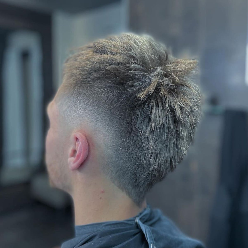 Side profile of a classic burst fade mohawk haircut featuring short, textured hair on top with a clean, sharp fade around the sides and back. The gradual burst fade enhances the contrast between the longer hair on top and the closely shaved sides, creating a bold, modern look.