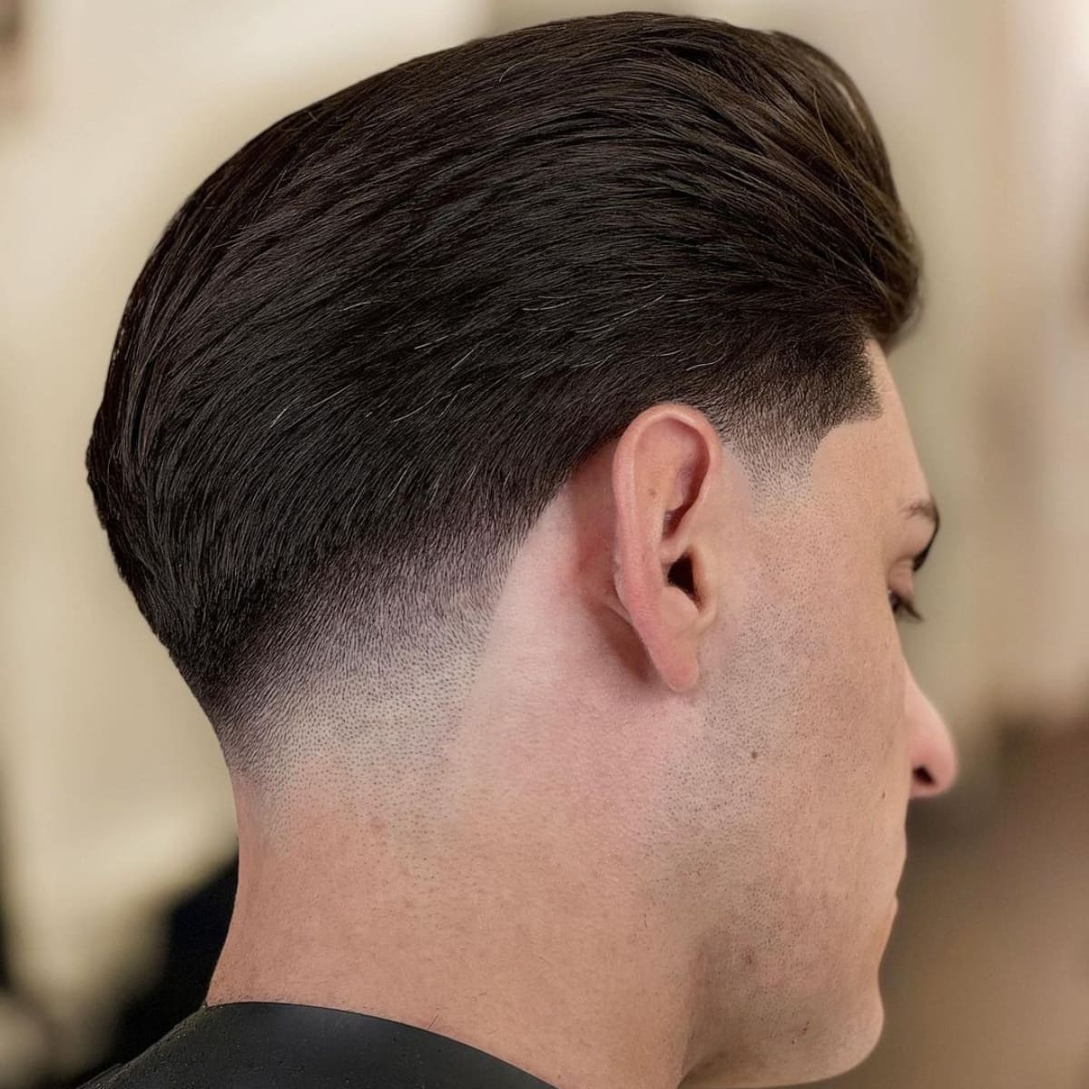 Side profile of a man with a smooth, voluminous hairstyle and a clean, tapered fade, showcasing a sharp, polished look from the neatly styled top to the perfectly blended neckline.