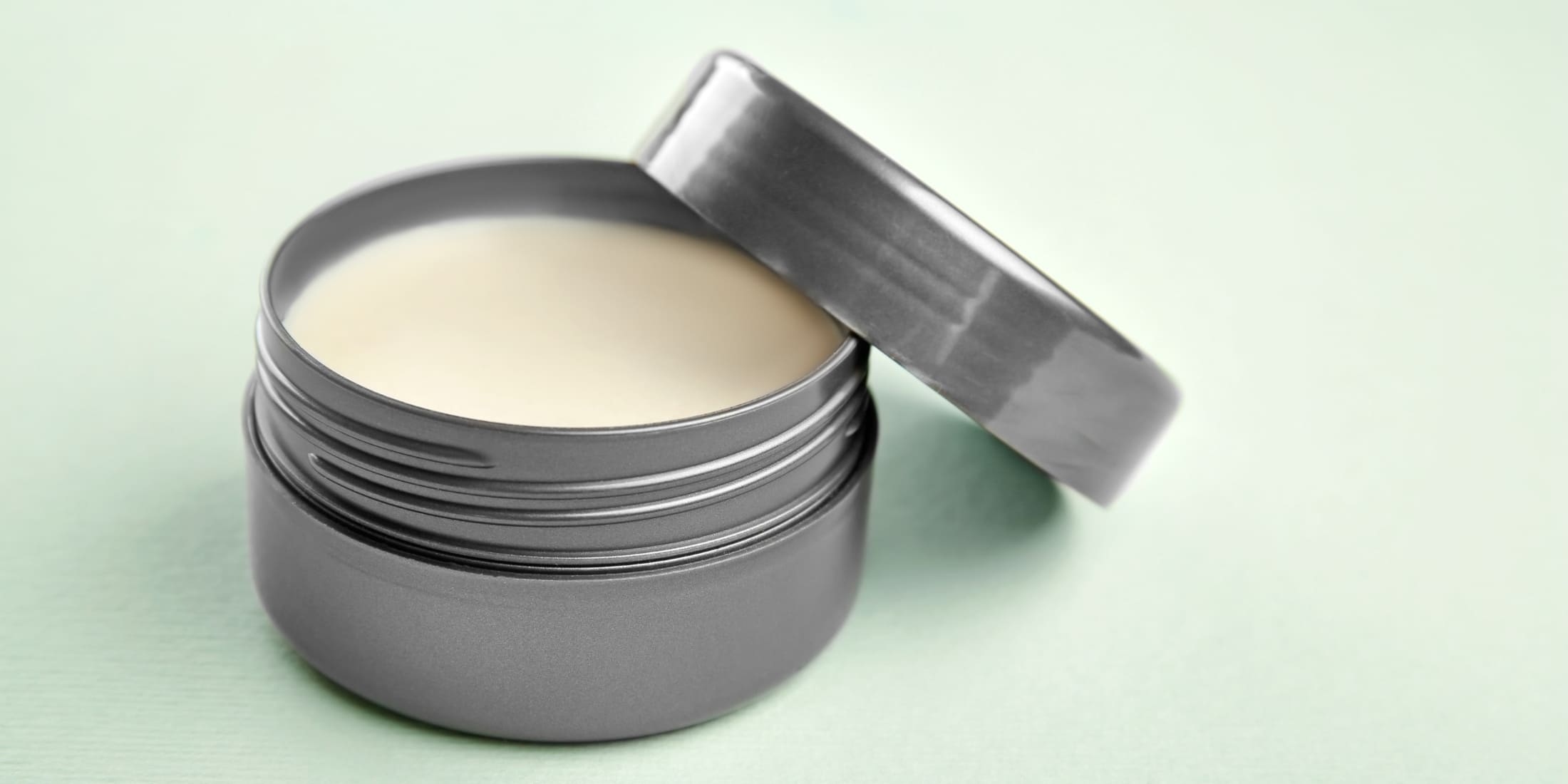 An open, sleek gray container of hair putty, showcasing its creamy texture. This image highlights what hair putty does by demonstrating its smooth consistency, ideal for styling hair without stiffness or greasiness. Perfect for understanding how to use hair putty to achieve a polished, manageable hairstyle.