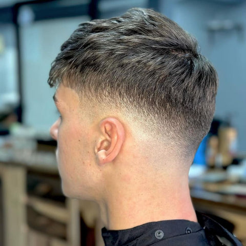 Close-up of a man with a fade hairstyle, showcasing a smooth gradient from longer textured hair on top to a clean, tapered fade at the nape. This is a versatile choice that blends traditional barbering with a modern, sleek finish, ideal for a fresh and stylish appearance.