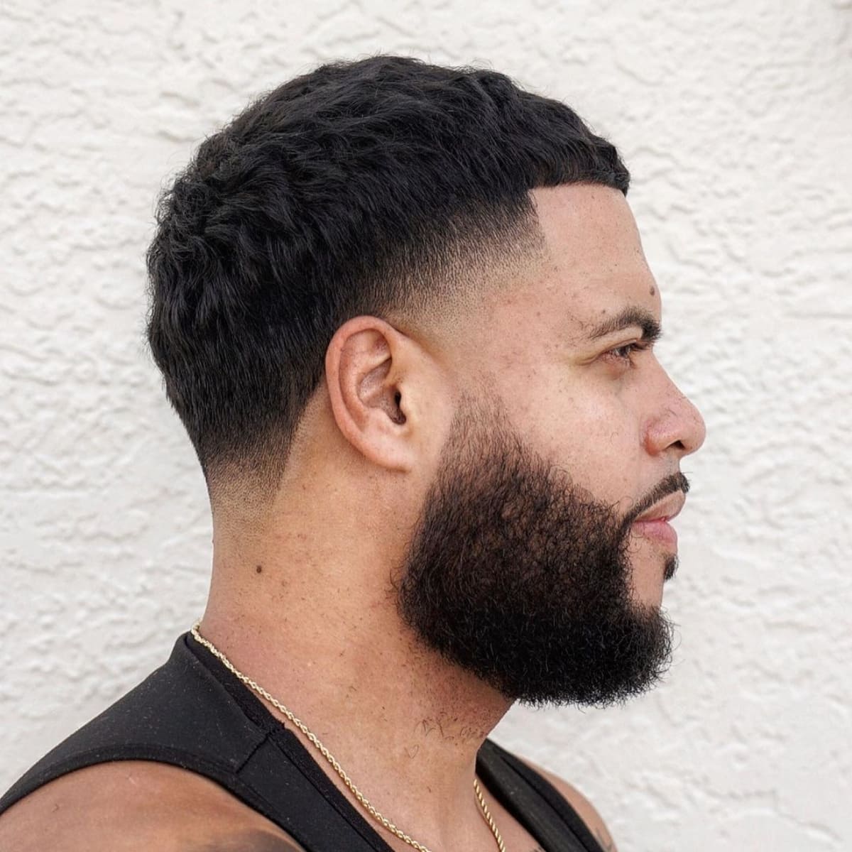 Side profile of a man with a stylish French Crop with Taper Fade haircut. The cut features a textured, cropped top with a smooth fade on the sides and back, transitioning seamlessly into a well-groomed, full beard. The combination of the sharp taper and bold beard creates a modern, clean look.