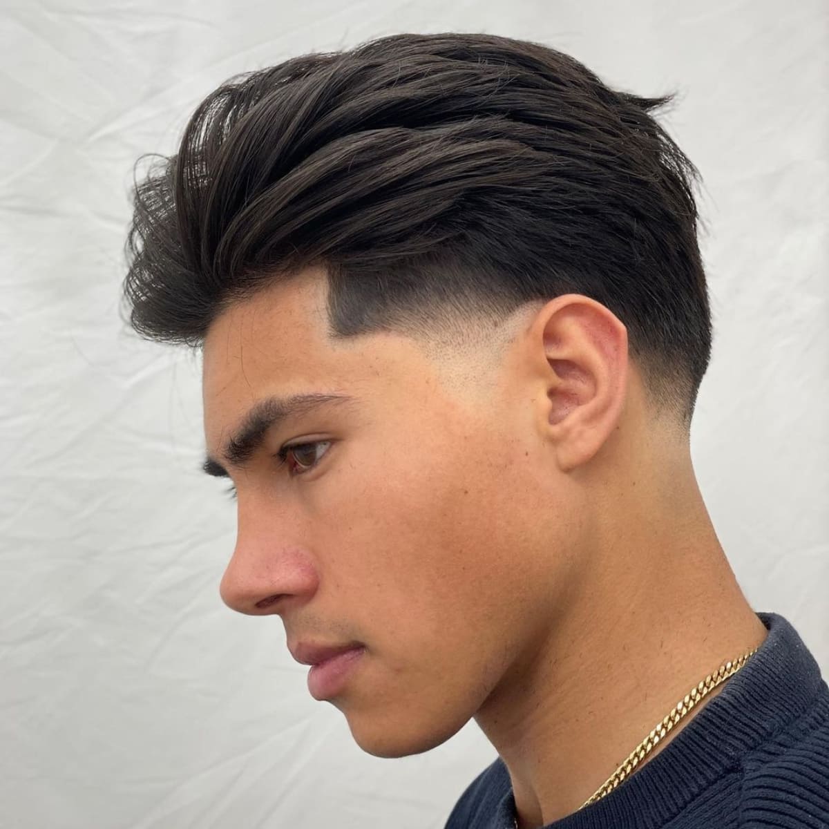 Side profile of a young man sporting a tapered slick back haircut. The voluminous top is paired with a sharp fade on the sides, creating a modern, clean look. The soft texture on top adds movement, while the tapered sides maintain a sleek, polished finish, making this style both versatile and stylish.