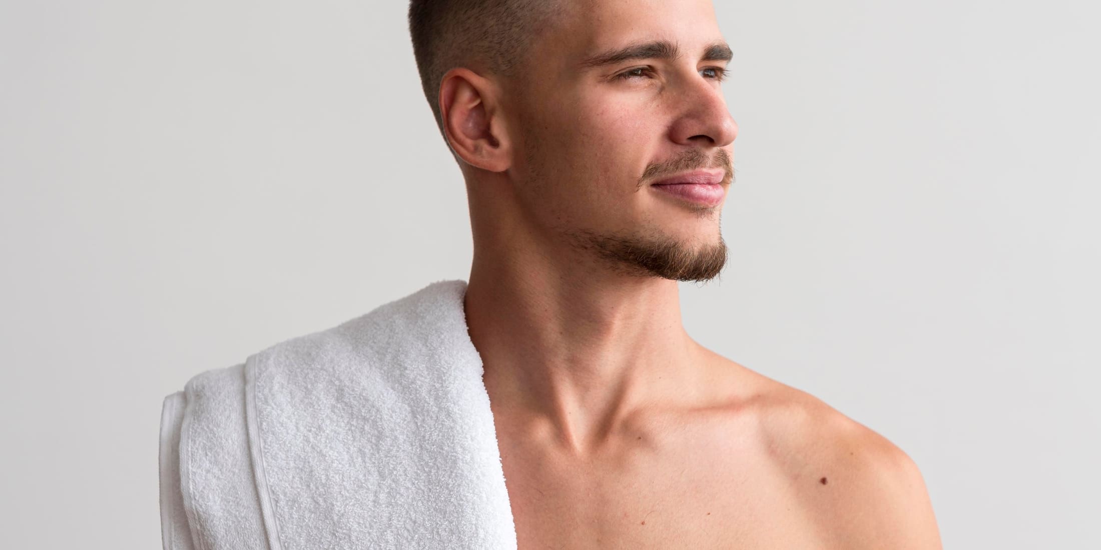 Confident young man with a towel over his shoulder, ready for manscaping below the belt.