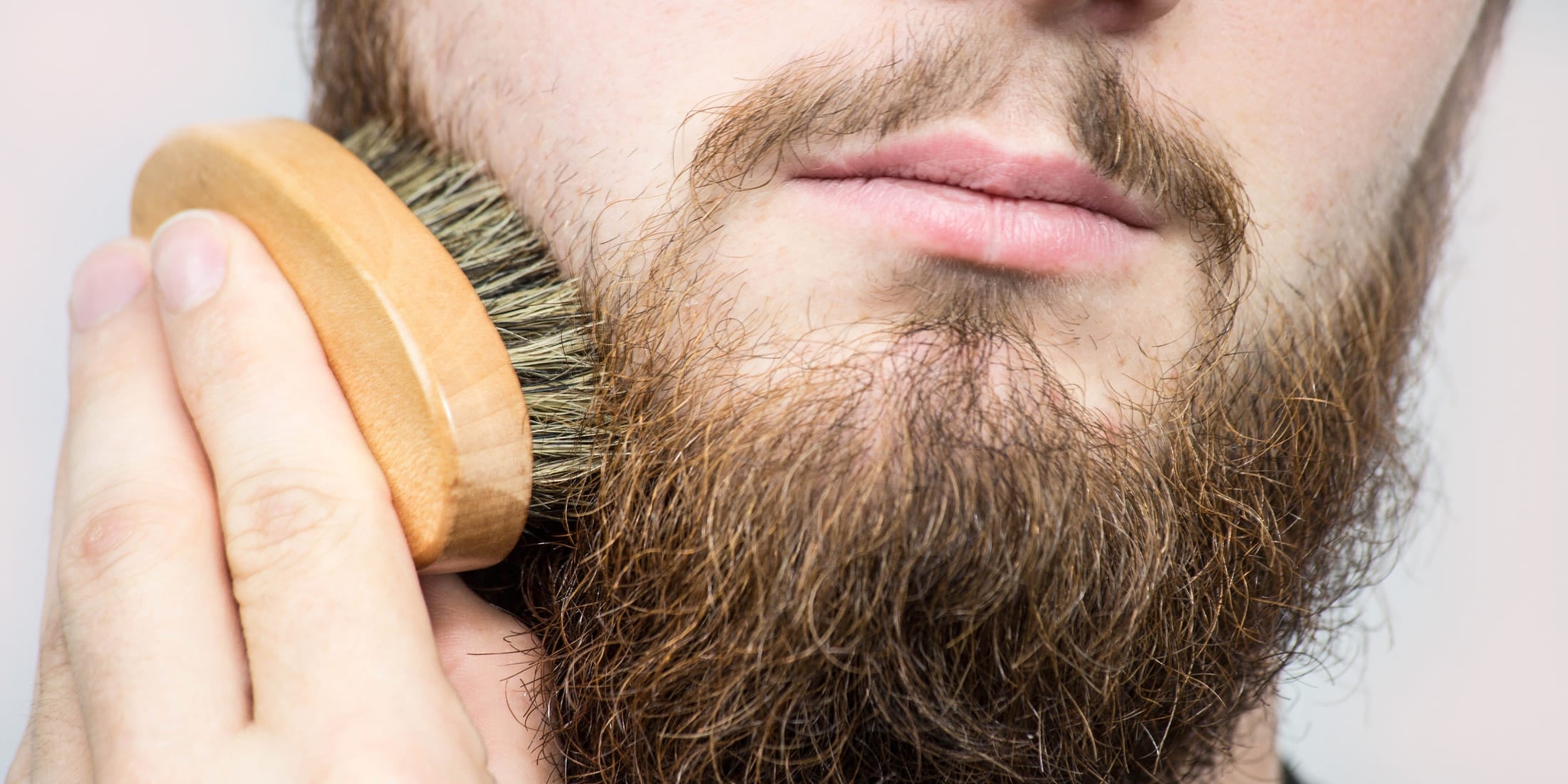 Man brushing his beard with a boar bristle beard brush, promoting healthy beard growth and even distribution of natural oils. Benefits of brushing your beard include enhanced appearance, reduced tangles, and improved skin health. Discover how brushing can help your beard grow and maintain its shape.