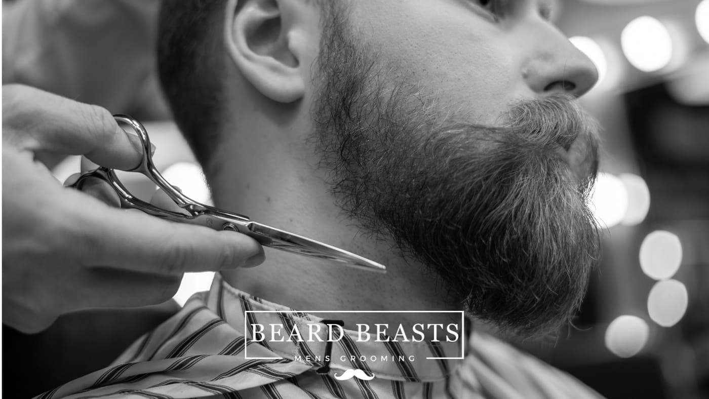 Man getting his beard professionally trimmed at a barbershop, demonstrating how to maintain a beard.