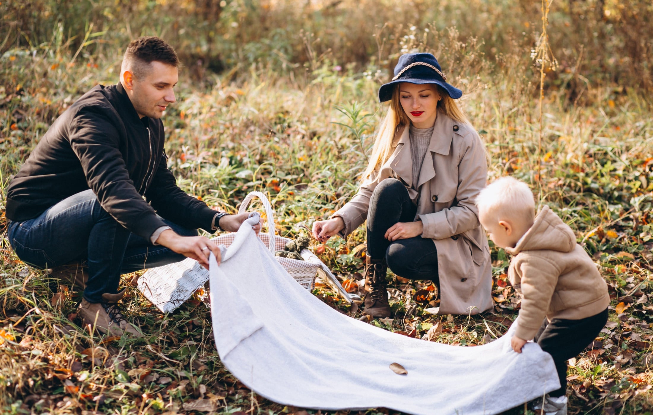 Family enjoying a picnic outdoors, with a father laying out a blanket, embracing quality time and self-care through family bonding in nature.