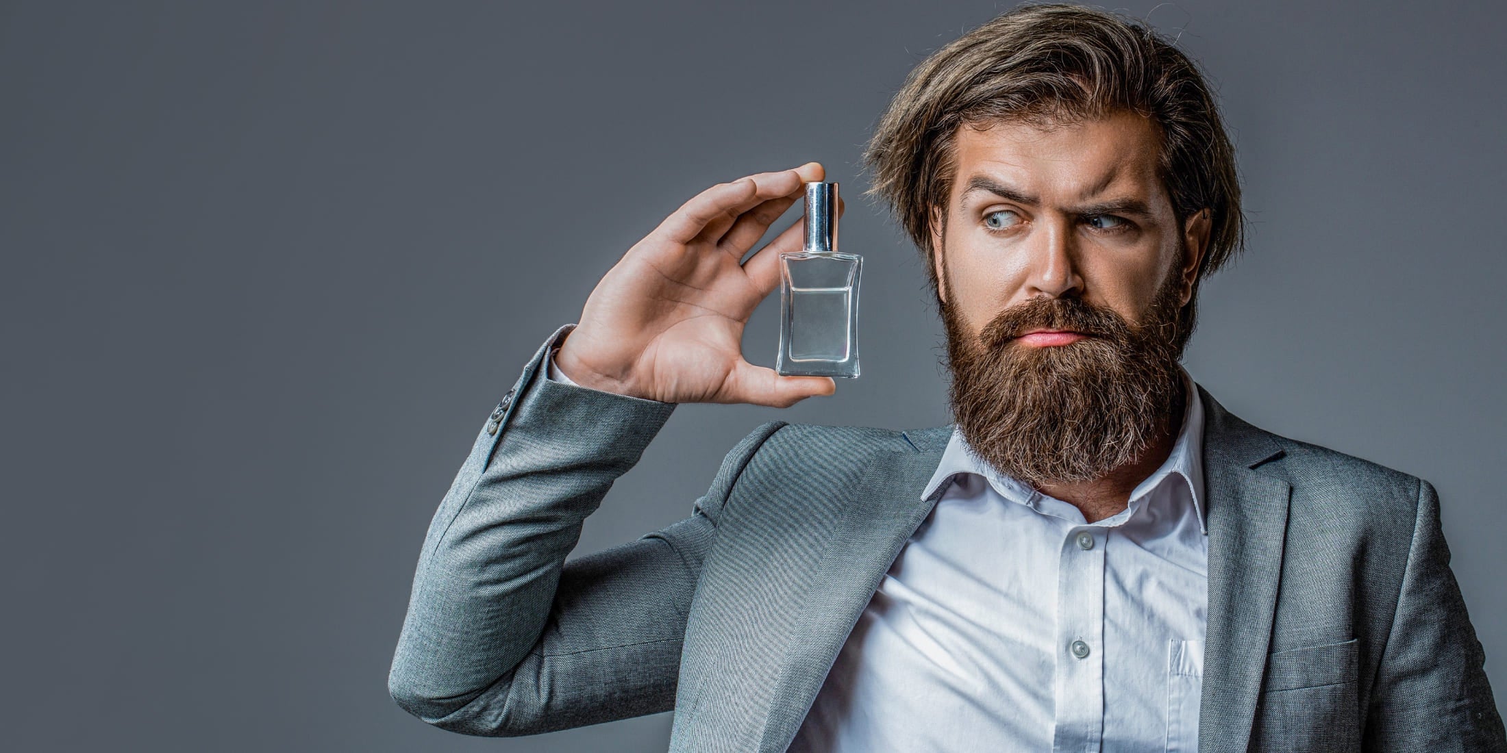 A man thoughtfully examining a bottle of cologne, considering scent options and cologne tips on how to smell better as a man.