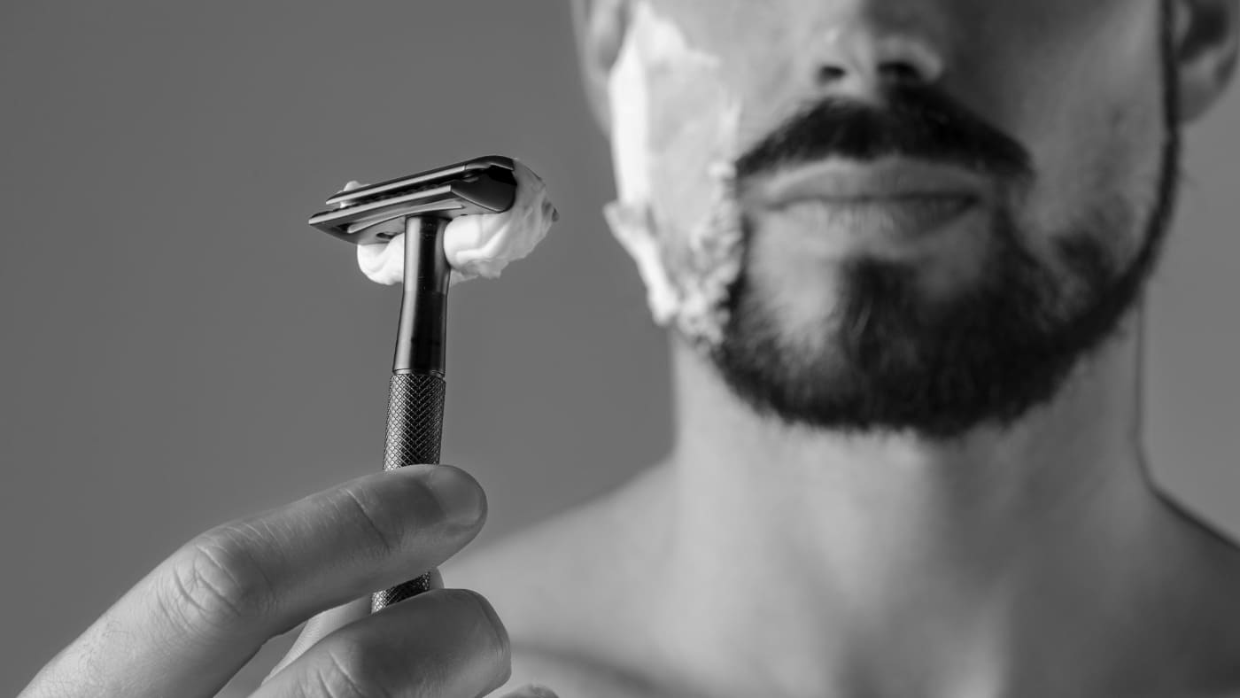 Man holding a safety razor, considering prevention of razor burn with shaving cream applied