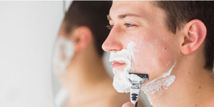 Man practicing wet shaving with shaving cream and razor, demonstrating what is wet shaving in front of a mirror