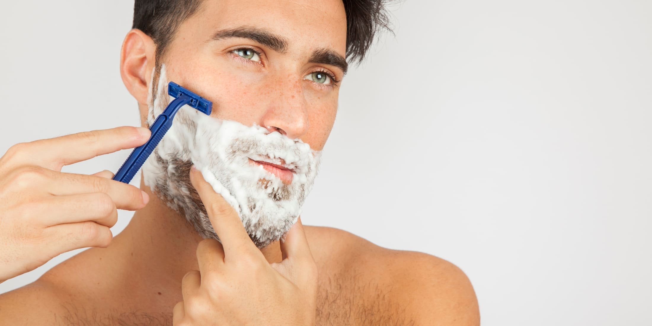 Man practicing wet shaving with shaving cream and a blue razor, demonstrating the traditional shaving technique