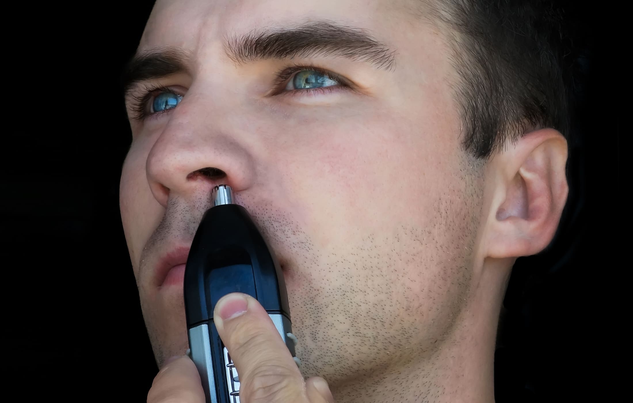 Close-up of a man using a nose hair trimmer to groom and maintain a neat appearance. The man looks focused, demonstrating the use of a quality grooming tool for hard-to-reach areas.