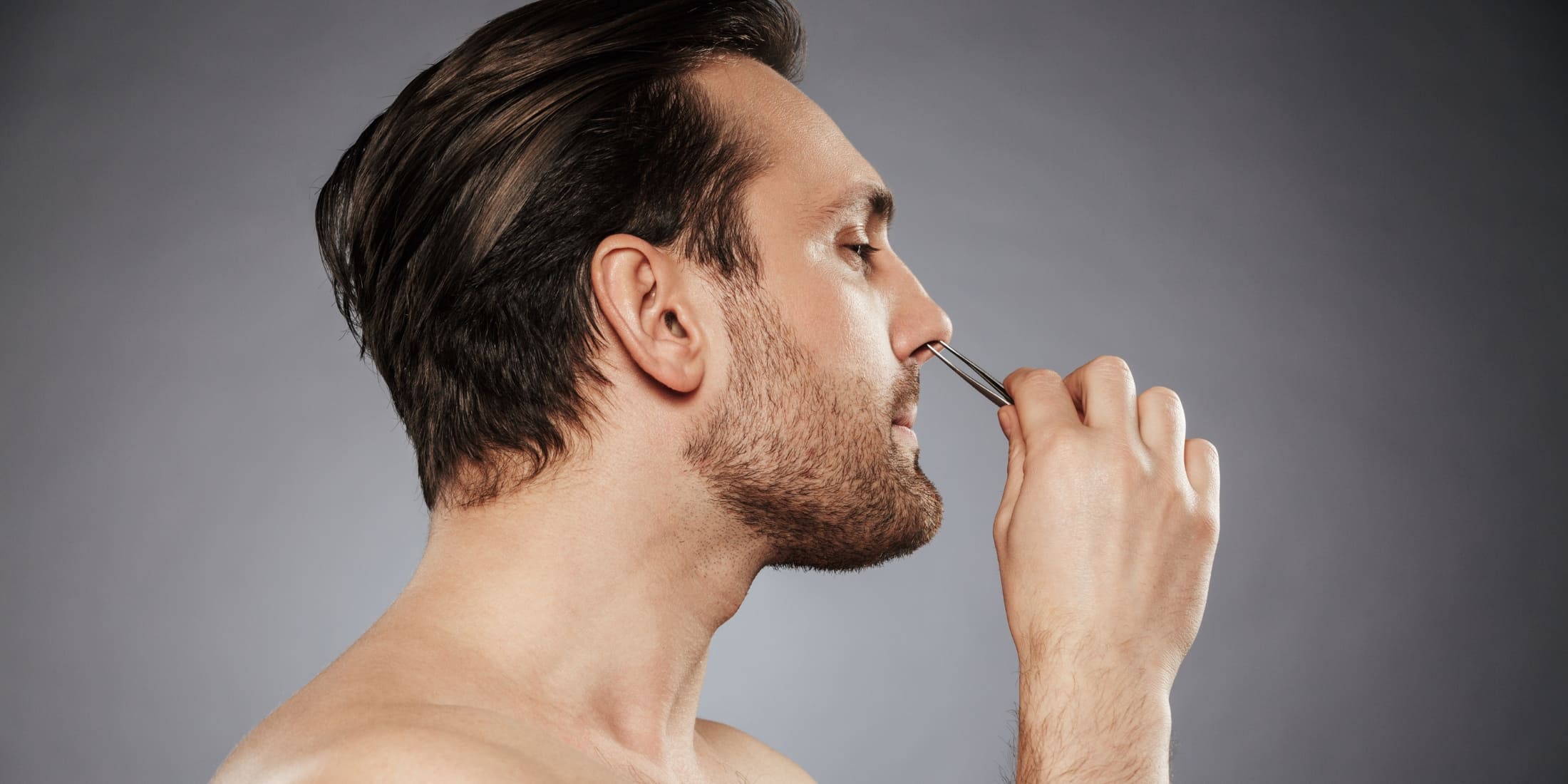 A man using tweezers to remove excess nose hair, highlighting the importance of grooming and hygiene tips for men. The image emphasizes maintaining a well-groomed appearance by trimming nose hair as part of a regular grooming routine for a polished, clean look.