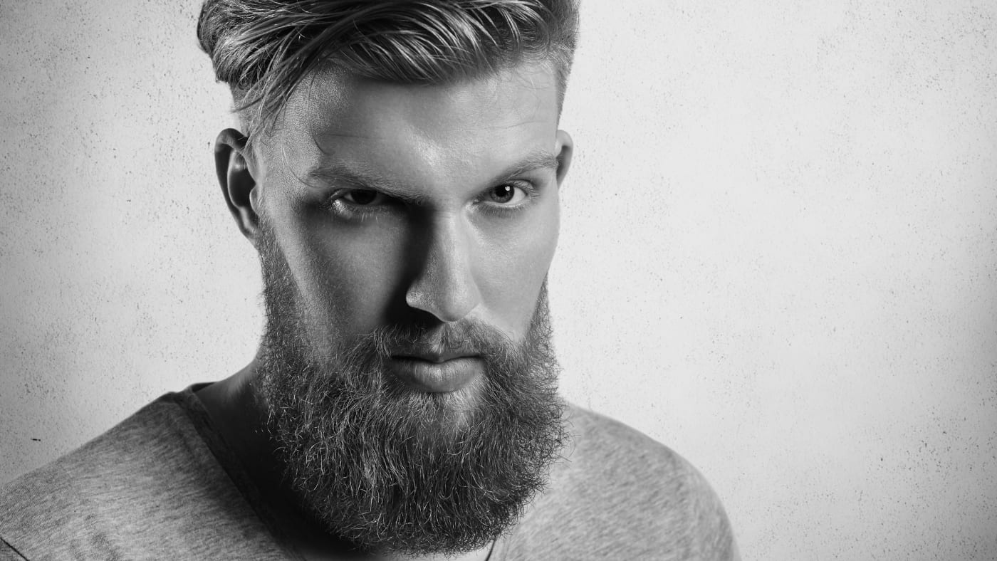 Stylish young man with a full, thick beard beyond the 2 month beard and modern undercut hairstyle in a monochrome portrait.