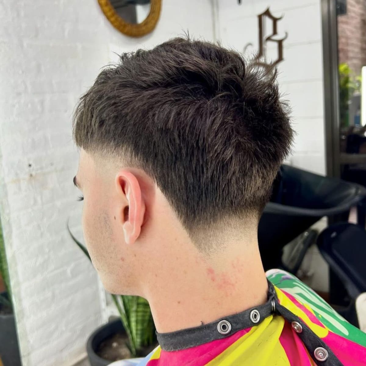 Back view of a man with a stylish haircut featuring a textured, short top and a gradual fade that transitions smoothly down the sides and nape. The clean fade and textured crown give the look a fresh, modern feel.