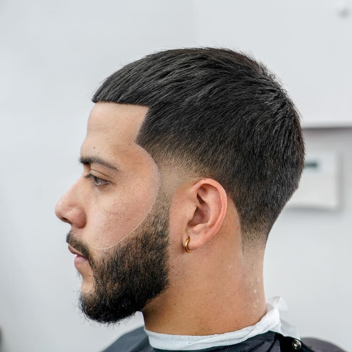 Side profile of a man with a clean and sharp French Crop with Taper Fade hairstyle. The cut features a neat, short cropped fringe and a smooth fade from the sides and back, creating a sleek and modern look. The style is paired with a well-groomed beard, enhancing the overall sharp appearance