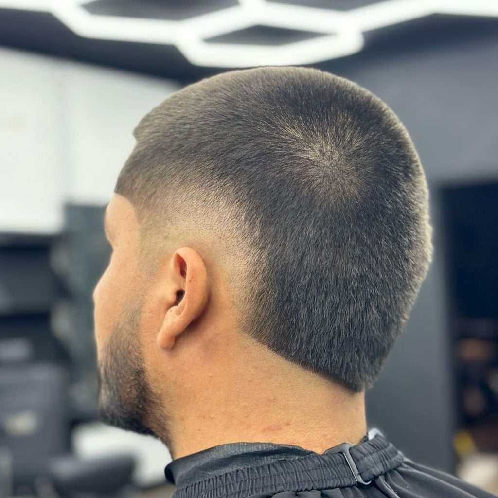 Back view of a man with a low burst fade buzz cut, showcasing a smooth, tapered fade around the ears and neck with closely trimmed hair on top for a sleek, modern look.