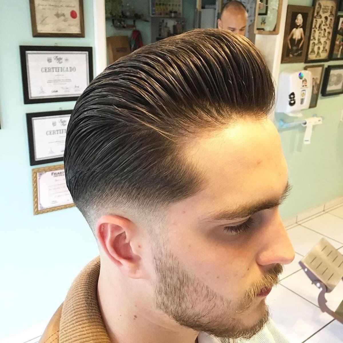 Close-up of a man sporting a low fade pompadour with a neatly groomed beard, showcasing a sleek, voluminous top and clean fade on the sides.