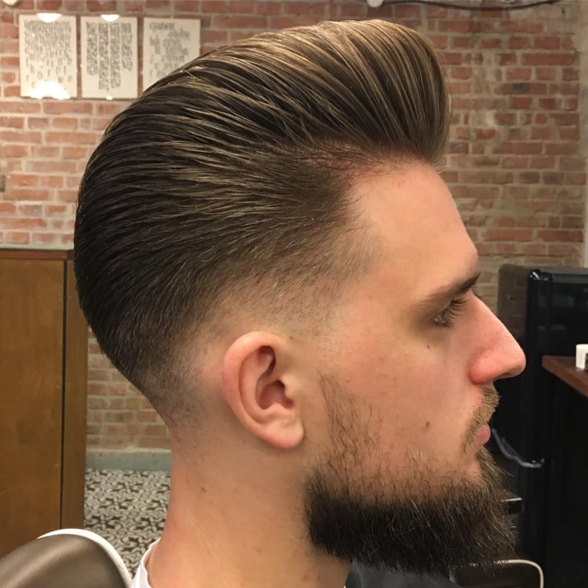 Side view of a man with a sleek low fade pompadour hairstyle, featuring a voluminous top and neatly tapered sides. Ideal for modern, stylish looks.