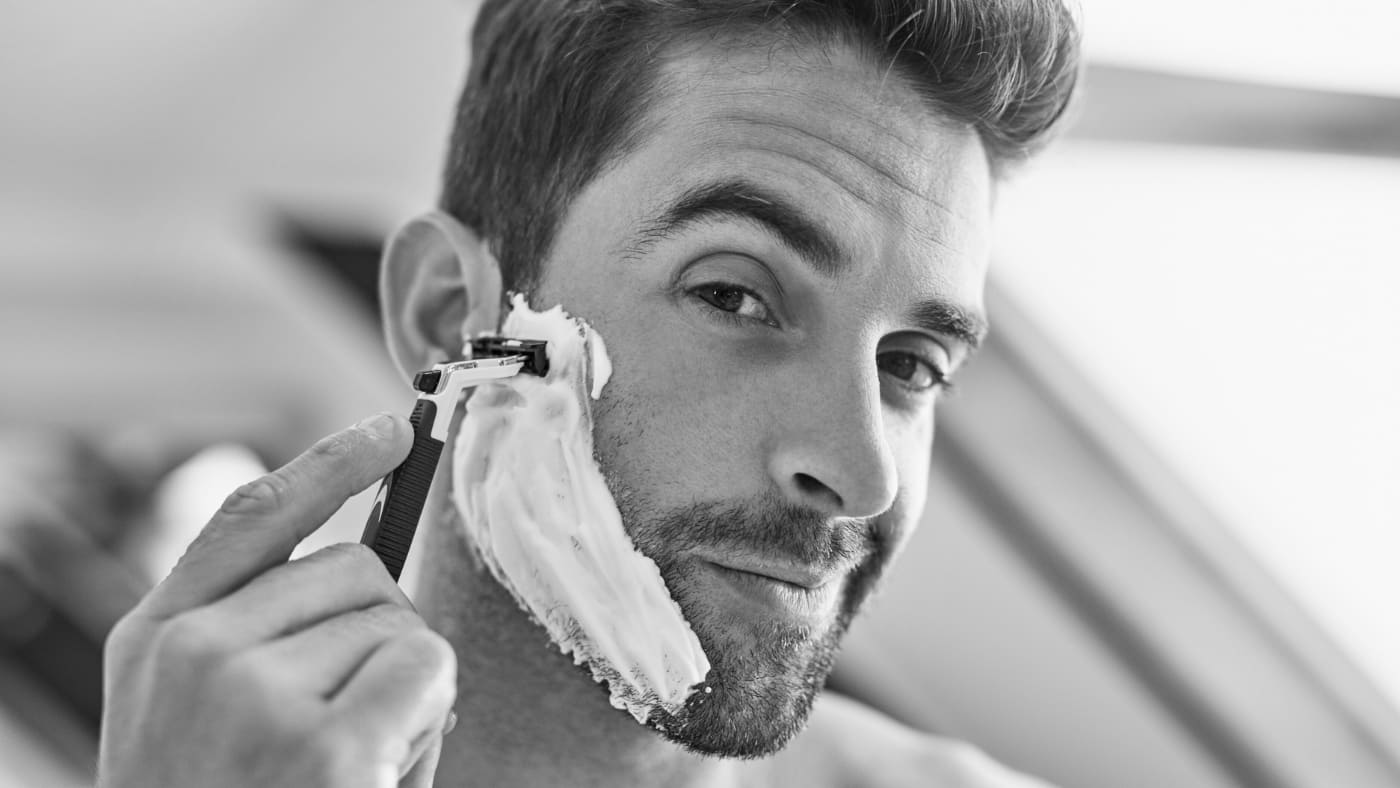 A man with shaving cream on his face using a razor, careful to avoid razor bumps.