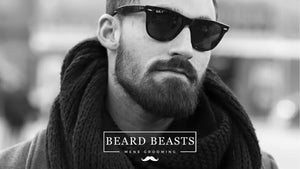 A man sporting a medium boxed beard, wearing sunglasses and a knitted scarf, posing for a men's grooming brand called Beard Beasts.