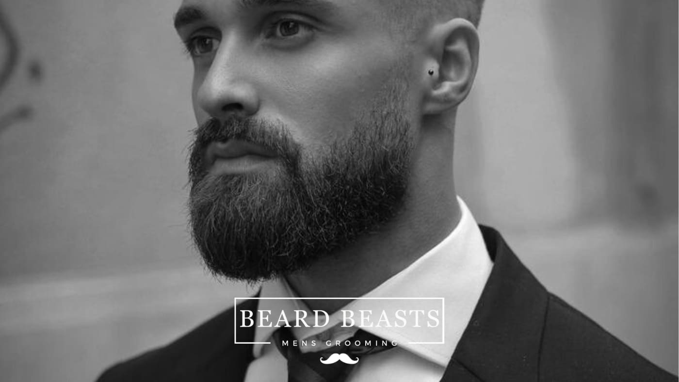 A well-groomed man in a suit, showcasing a stylish medium boxed beard, featured in a black and white photo for Beard Beasts Men's Grooming.