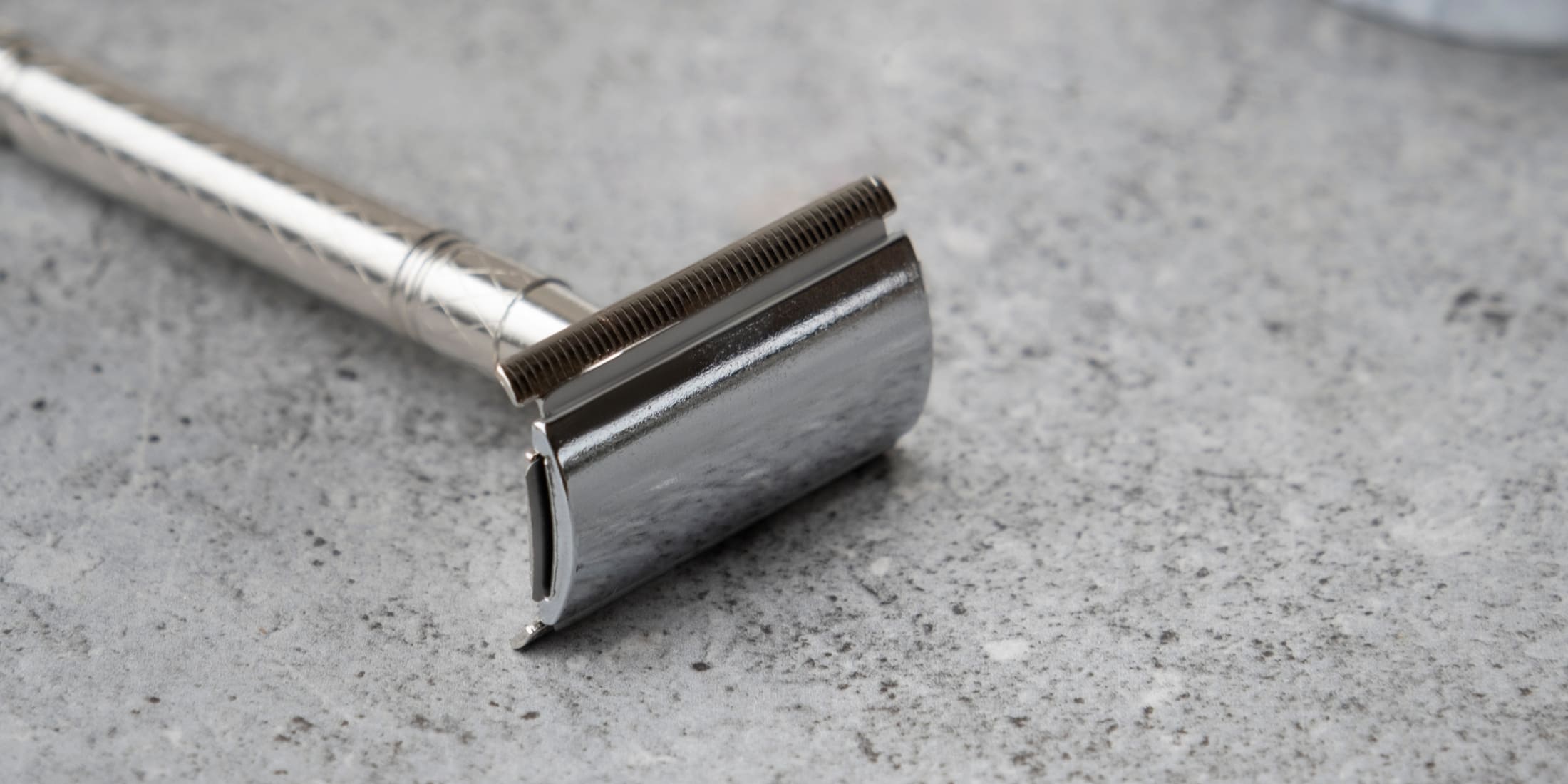 Close-up of a safety razor placed on a marble countertop. The image showcases the razor's clean, polished metal finish, highlighting its design and craftsmanship, essential for a smooth shaving experience.