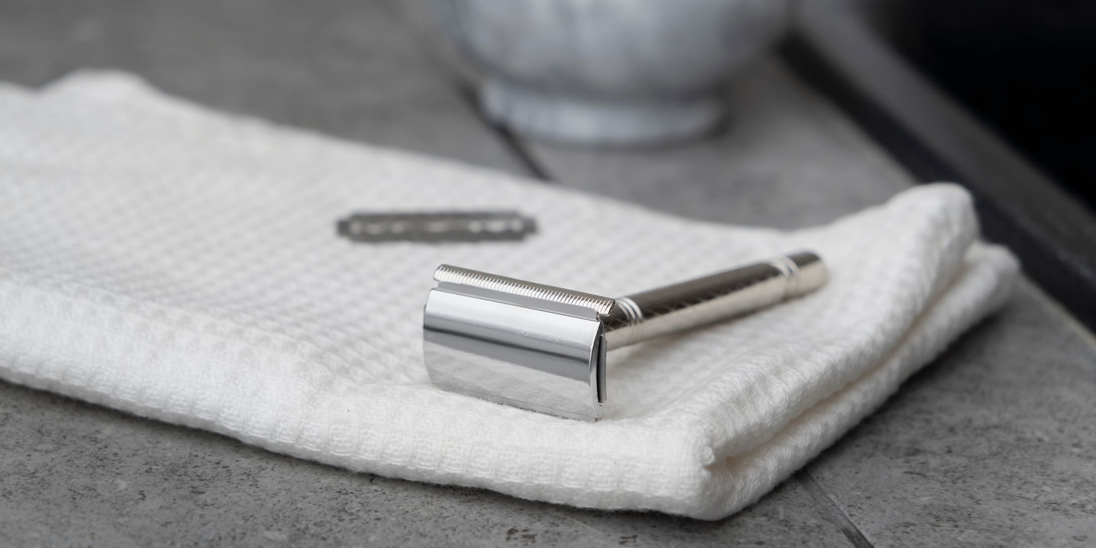 Safety razor resting on a white towel with a razor blade in the background. The clean, polished razor and soft towel emphasize how to clean a safety razor properly for a smooth, hygienic shave.