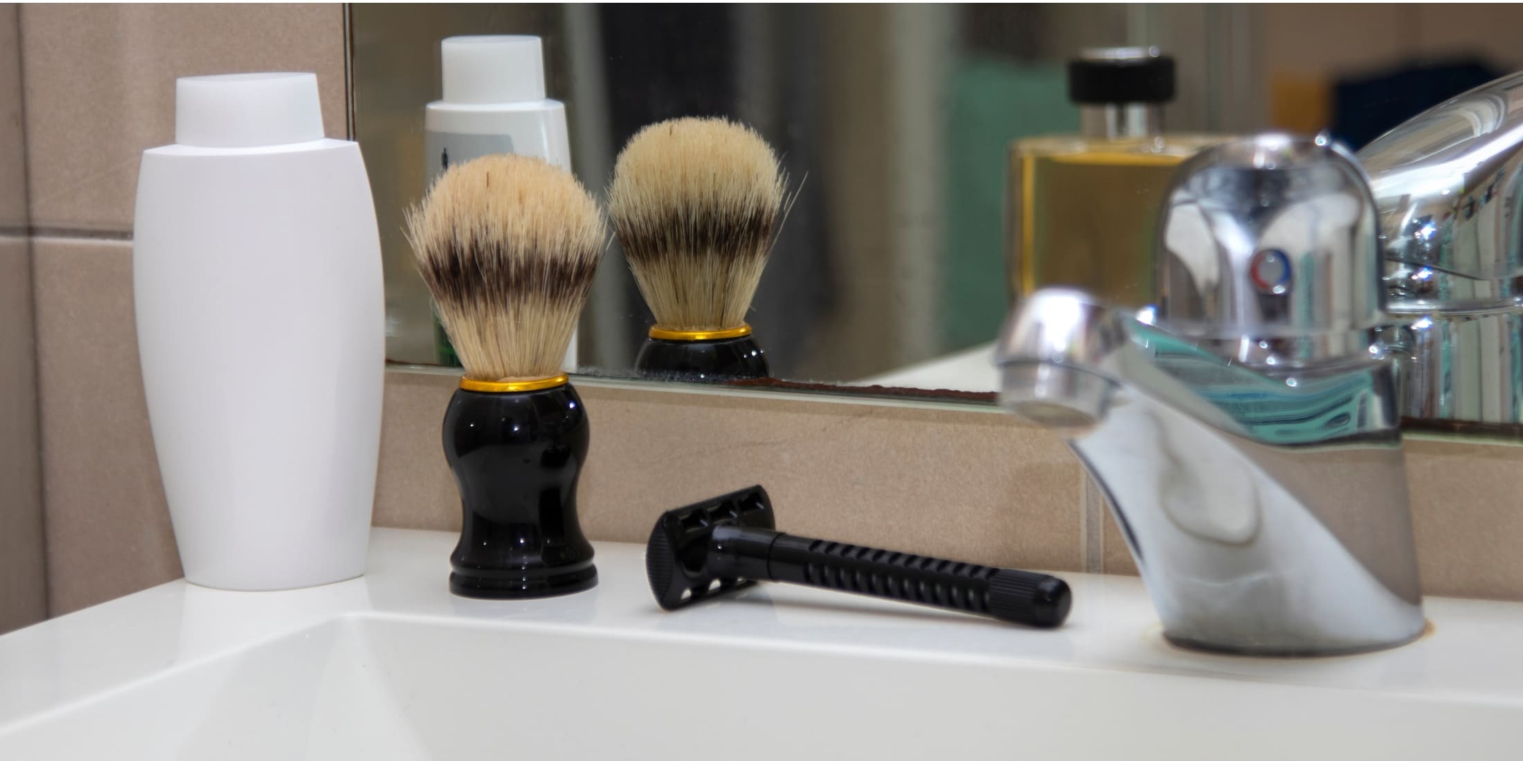 Shaving brush with a black handle placed on a bathroom sink next to a razor and toiletries, reflecting the importance of proper grooming. Learn how to clean a shaving brush for optimal hygiene and performance.