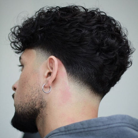 Rear view of a man with a taper hairstyle, featuring naturally curly hair on top transitioning smoothly into a clean, gradual taper fade. This classic men's hairstyle is ideal for those seeking a stylish, low-maintenance look that enhances natural texture while providing a polished finish.