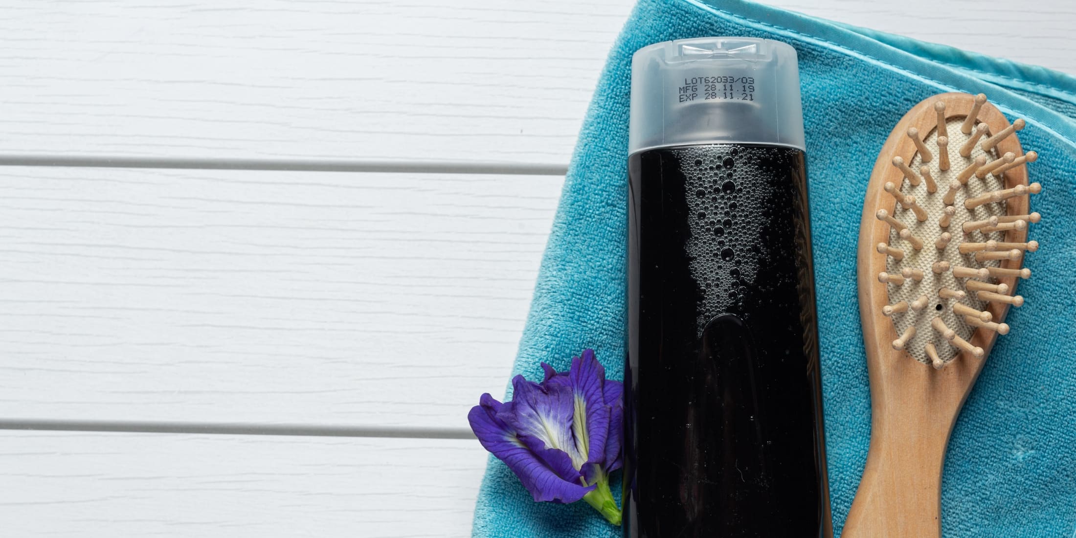 Tube of men's hair gel placed on a blue towel with a wooden hairbrush and a purple flower, highlighting hair styling options and the difference between pomade vs gel.