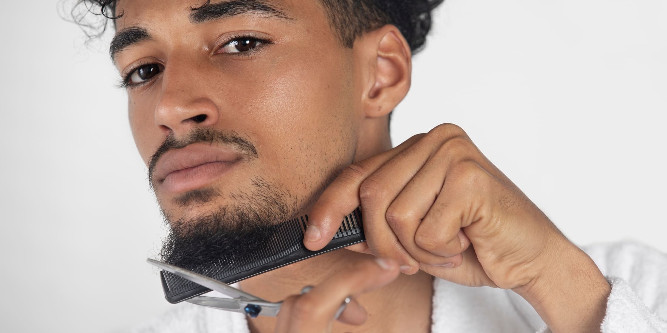 Young man trimming his short beard using a comb and scissors. This image demonstrates short beard grooming techniques, highlighting how to maintain, trim, and shape a short beard for a neat and stylish appearance.