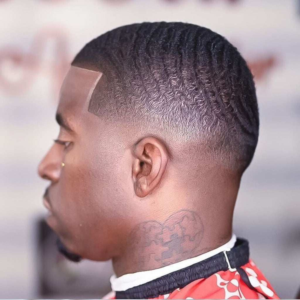 Side profile of a man showcasing a clean and stylish bald drop fade haircut paired with perfectly defined 360 waves. The haircut features a sharp lineup at the hairline, seamlessly transitioning into the smooth fade around the sides and back. The waves are neatly contoured, highlighting the natural texture and precision of the style. A bold and polished look popular among Black men for its timeless appeal and cultural significance.