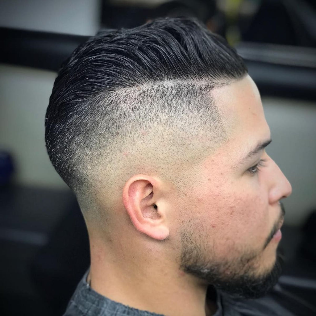 Side profile of a man with an undercut hairstyle featuring a sharp, clean fade. The longer top is styled back, creating a distinct contrast with the closely shaved sides, adding depth and definition to the look. The hairstyle combines a bold, edgy undercut with a smooth fade for a modern and polished appearance.