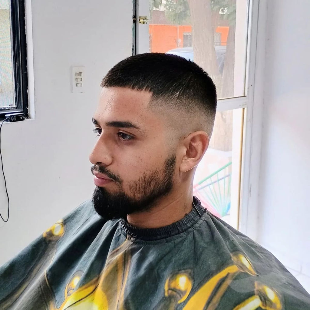 Man with a stylish bald high fade haircut featuring a clean, sharp transition from longer top hair to shaved sides, highlighting a neatly trimmed beard. This modern bald fade hairstyle emphasizes contrast, adding a bold, structured look suitable for a fashionable, low-maintenance style.