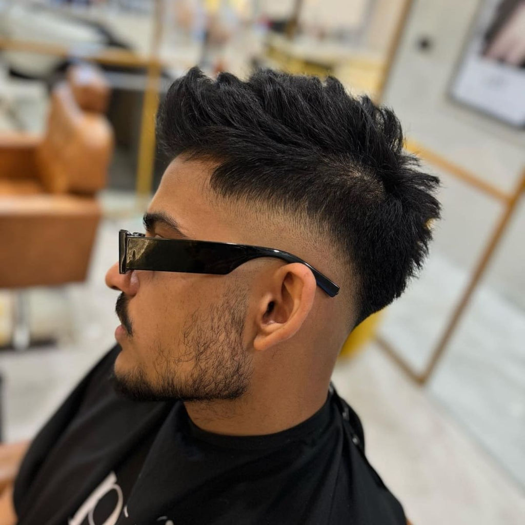 Side profile of a man with a mid fade haircut, showcasing a smooth transition from a full, textured top to a closely shaved fade around the middle of the head. The hairstyle adds volume on top, styled upward for a dynamic, modern look, while the fade enhances the clean lines and contrasts sharply with the longer hair. Paired with stylish sunglasses, this look offers a trendy, confident vibe.