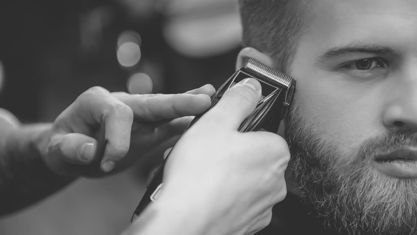 Close-up of a barber using clippers to give a customer a precise #6 buzz cut, complemented by a well-groomed beard.