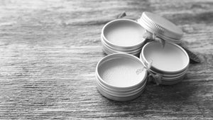 Comparison of open containers of mustache wax and beard balm on wooden surface, highlighting differences in texture and application