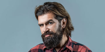 Portrait of a man with a thick, well-groomed beard and long head hair, illustrating the differences between beard hair vs head hair. 