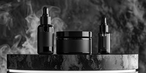 Beard oil vs beard balm comparison: sleek black containers of beard grooming products, including beard oil dropper bottles and a beard balm jar, displayed on a stylish black surface with a smoky background