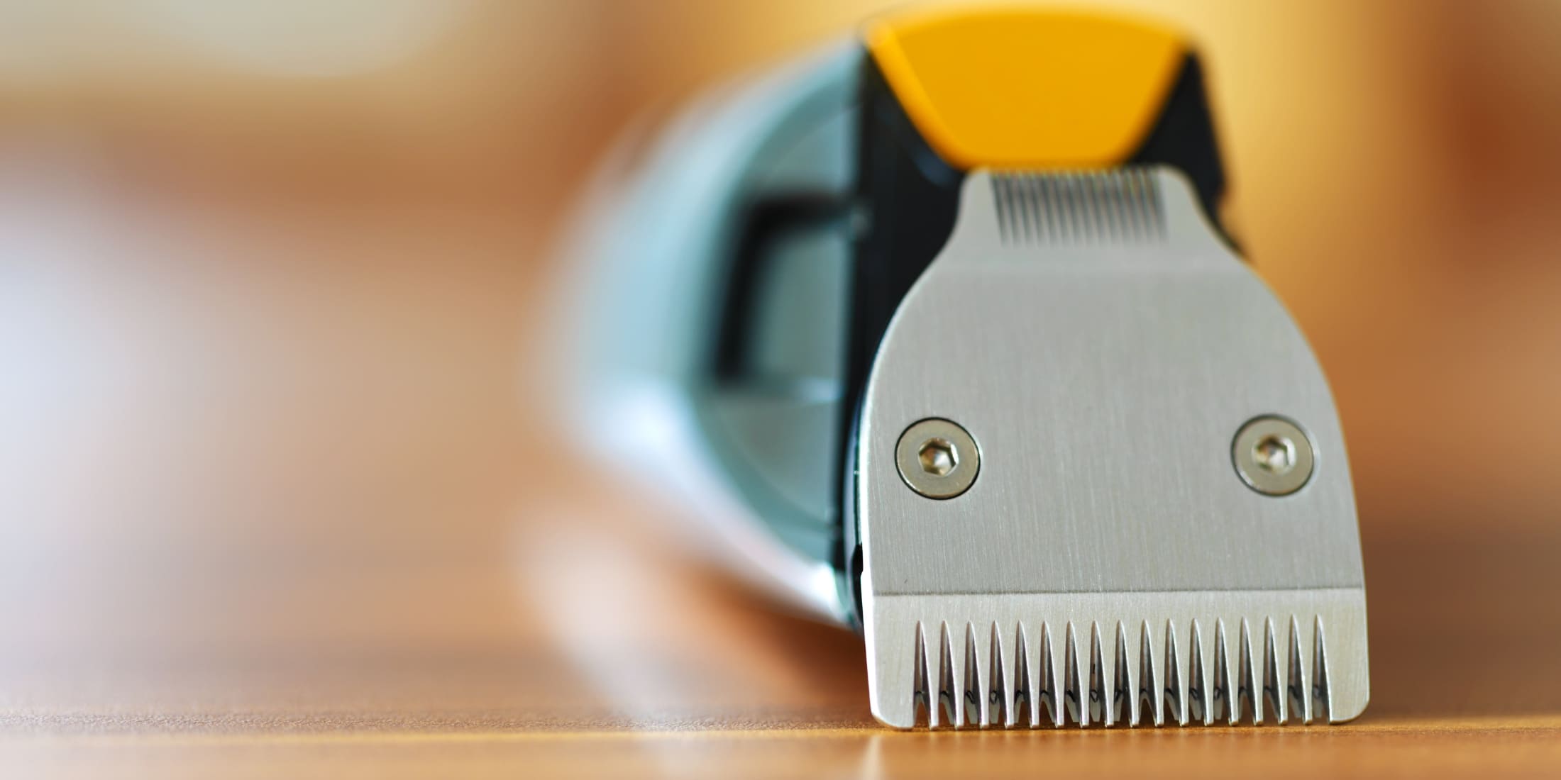 A close-up image of a beard trimmer, showcasing its sharp metal blades and sleek design. The trimmer, primarily grey with a yellow accent, is positioned on a wooden surface with a soft, blurred background, emphasizing the precision and quality of the tool, ideal for maintaining a 5mm beard.