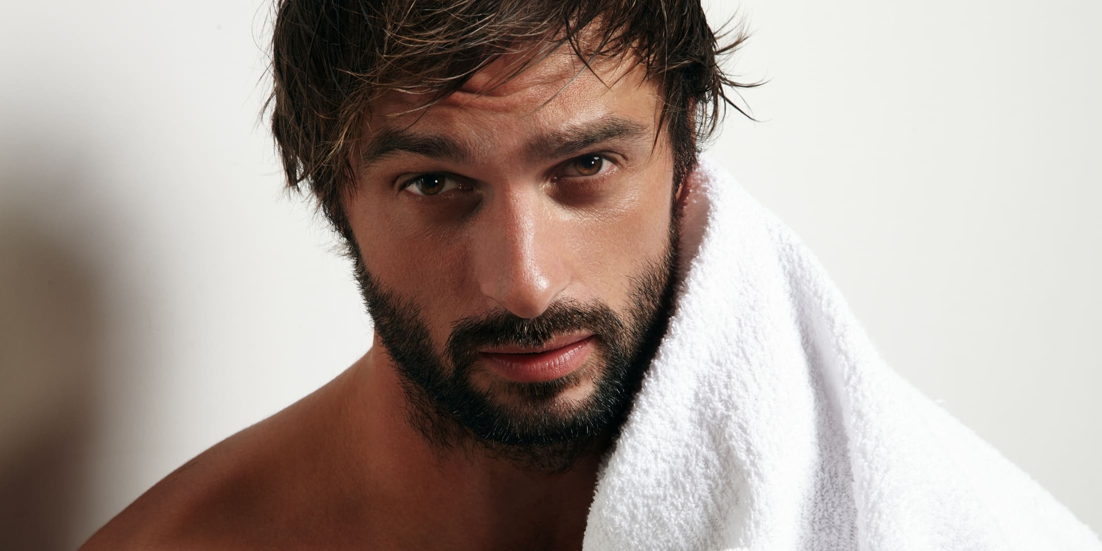 Handsome bearded man with a towel over his shoulder, showcasing a soft and well-conditioned beard after using beard conditioner.