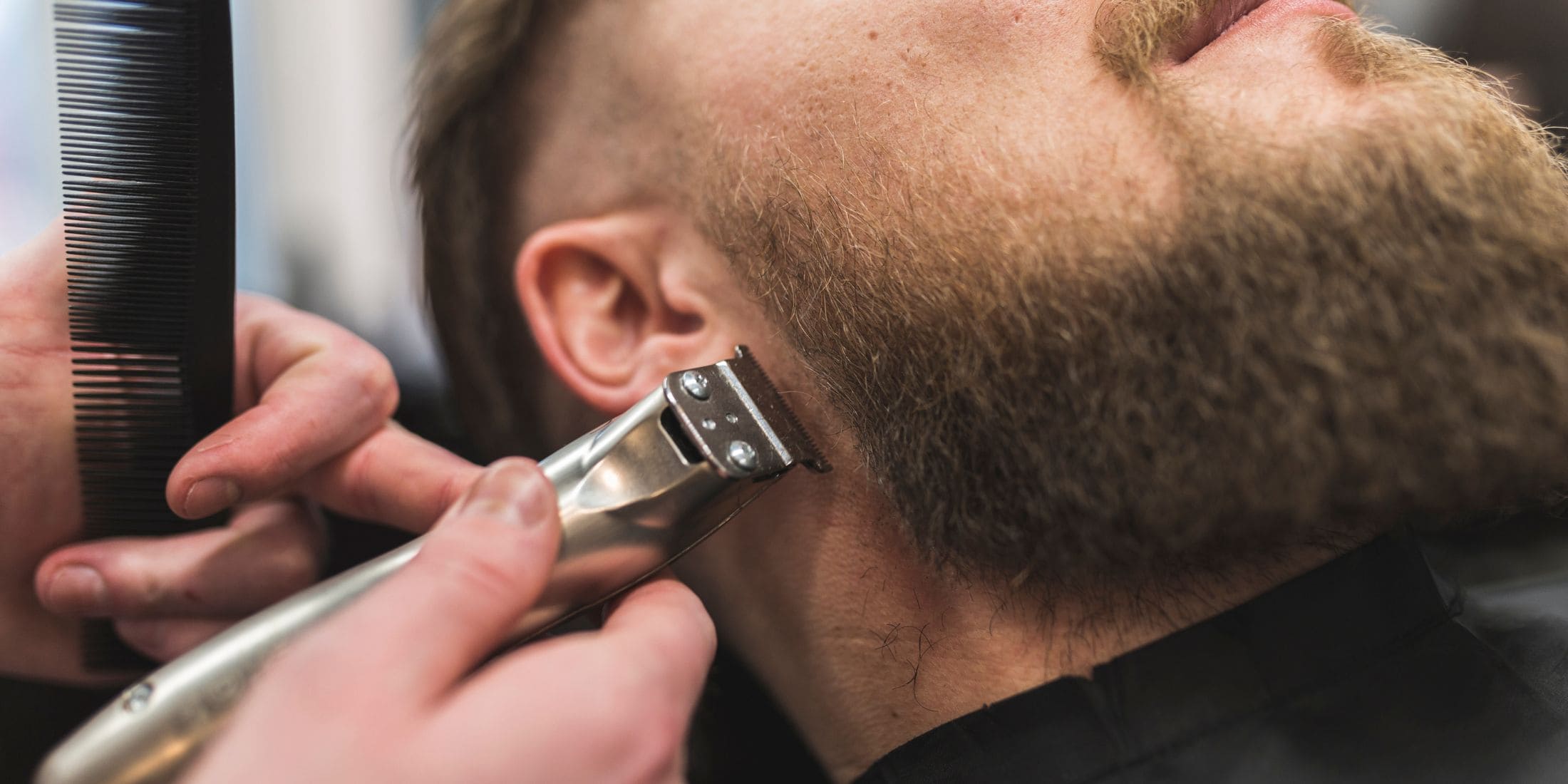 Barber carefully shaping a full beard with precision, using a comb and trimmer to create a sharp, defined look for a well-groomed appearance.