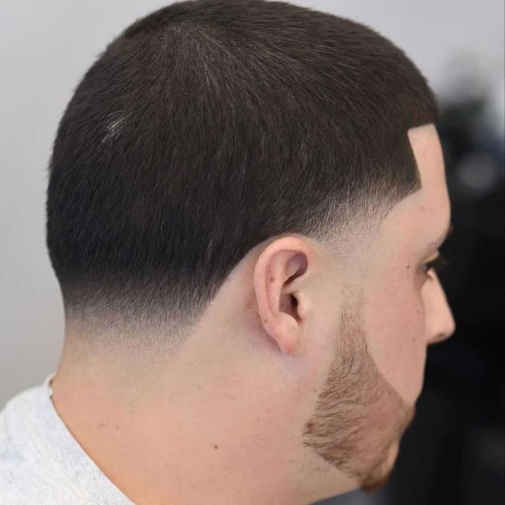 Side view of a man with a short cut featuring a smooth low taper fade that transitions gradually down the neck. The sharp beard line complements the clean, polished look, creating a well-groomed appearance.