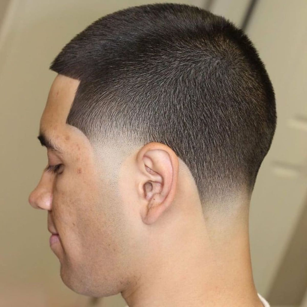 Side profile of a man with a buzz cut low taper haircut. The hair on top is cut short and even, while the sides and back feature a precise low taper fade, blending smoothly into the skin. The sharp, clean hairline highlights the sleek and polished look of the buzz cut low taper style.