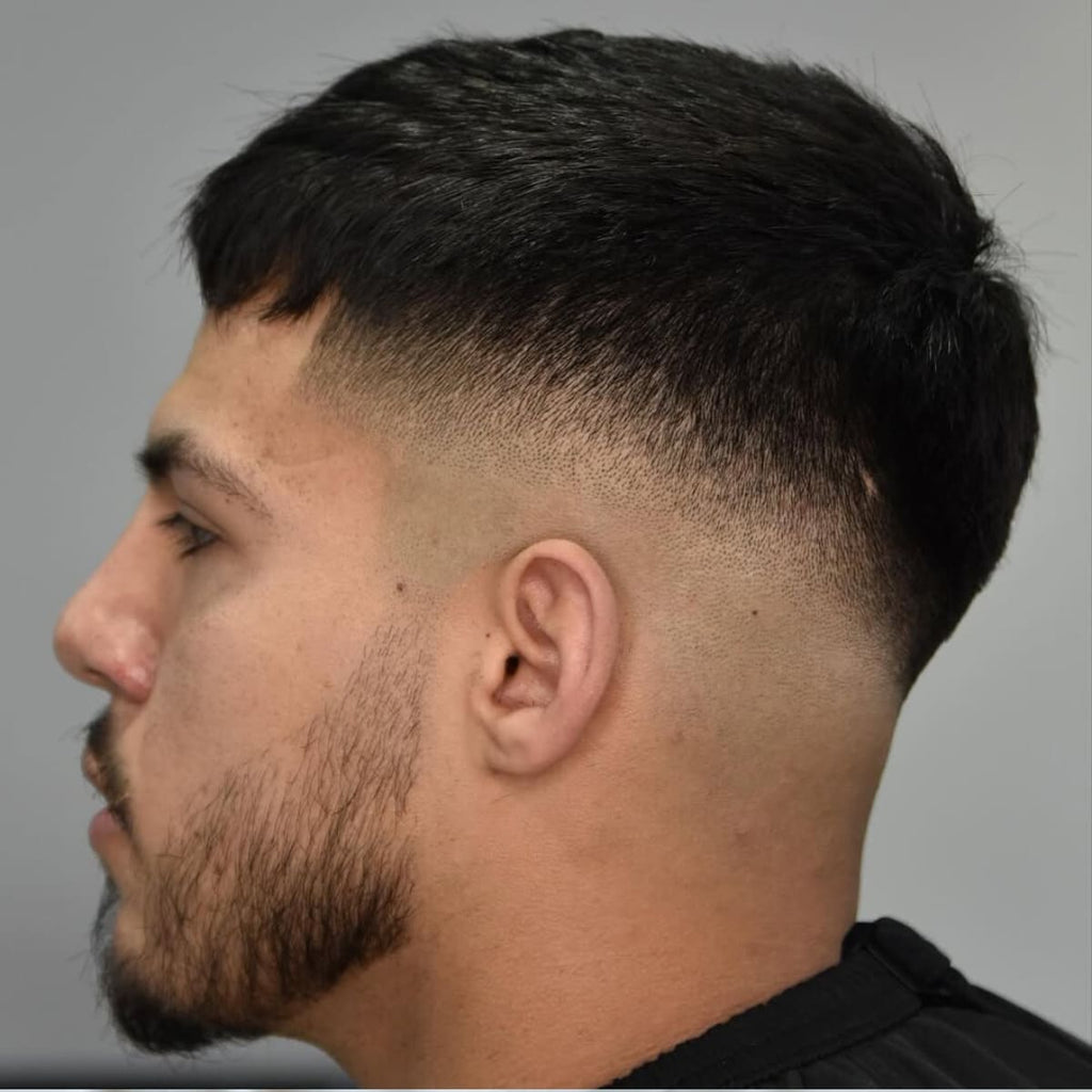 Side profile of a man with a clean and sharp bald drop fade hairstyle. The haircut features a smooth gradient from longer hair on top to a seamless skin fade that curves naturally around the back of the head. The style is paired with a short, well-groomed beard for a polished and modern look. Ideal for those seeking a versatile and trendy men's haircut.