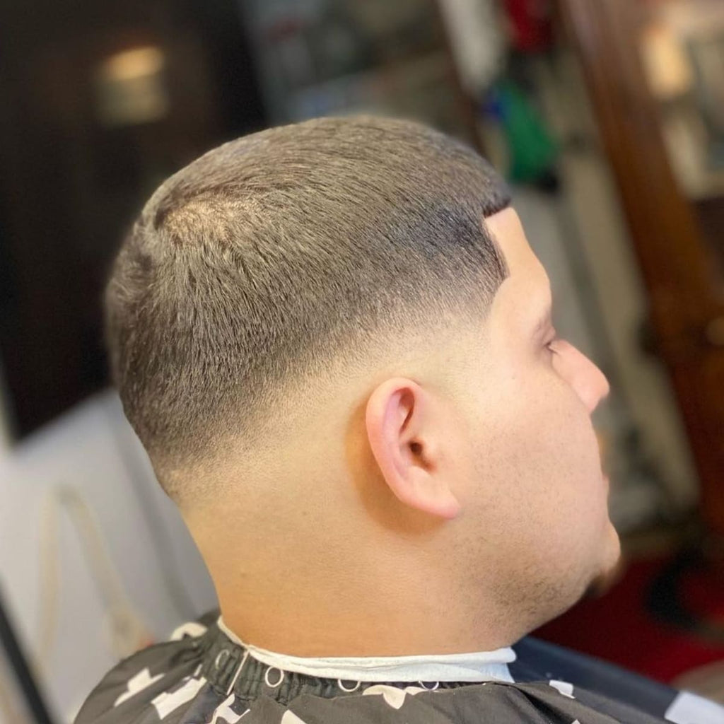 Side profile of a man with a classic mid fade buzz cut haircut, featuring a smooth, gradual fade that blends seamlessly from the short sides to a slightly longer top. The haircut is completed with a sharp hairline finish, giving a clean, polished look. Ideal for those seeking a low-maintenance, modern style that enhances facial structure.