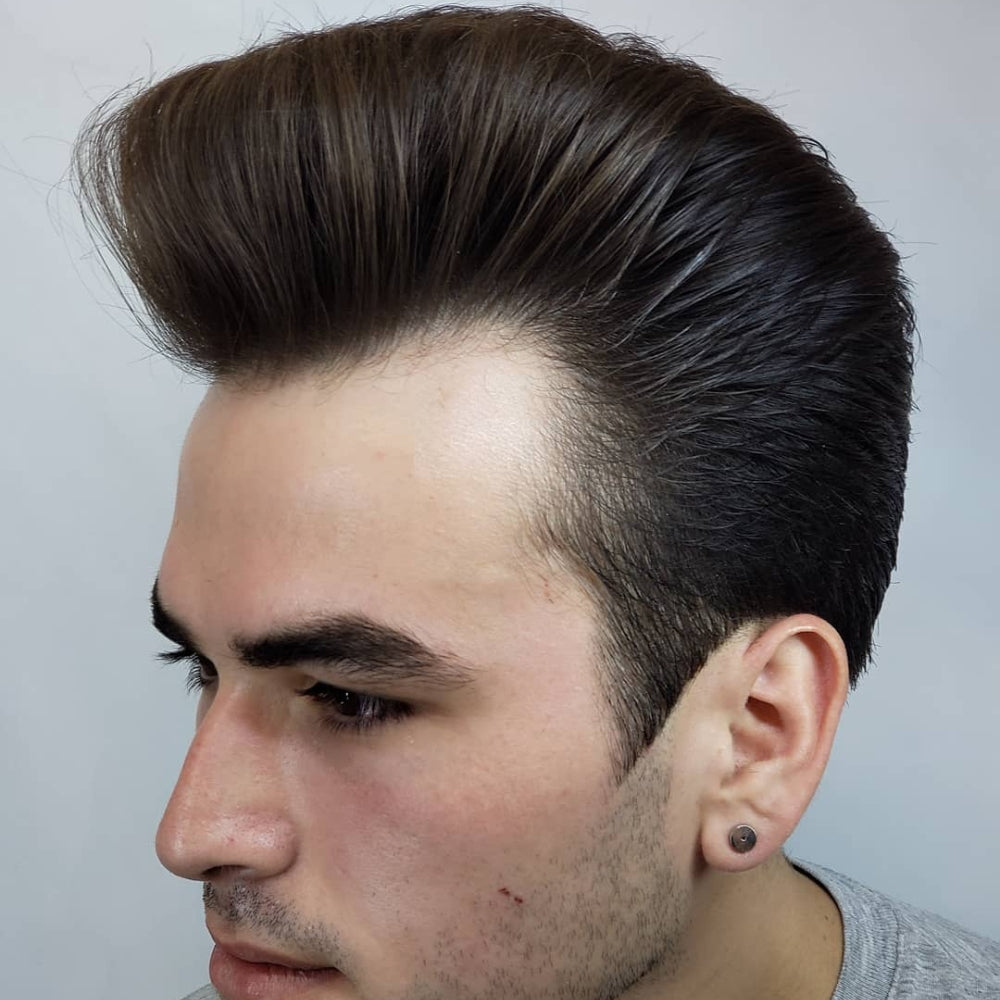 A young man is showcasing a classic pompadour haircut in this image. The sides are neatly trimmed, while the top hair is styled high and voluminous, creating an impressive and smooth wave. His hair is sleek and glossy, reflecting careful grooming and the use of quality hair products. The overall look is polished and elegant, emphasizing the timeless appeal of the classic pompadour. The man has a focused expression, and his skin is clear, further highlighting the sophistication of his hairstyle.